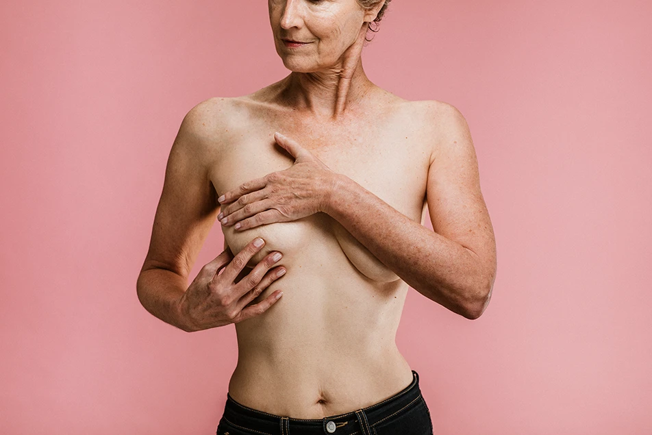 Mature, topless woman covering her chest with her hands and arms to represent consideration of a breast uplift procedure.