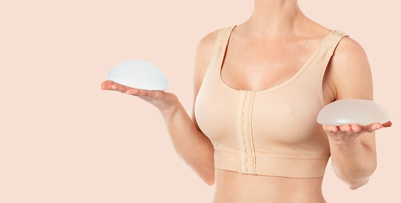 Woman wearing a post surgical bra holding a breast implant in each hand