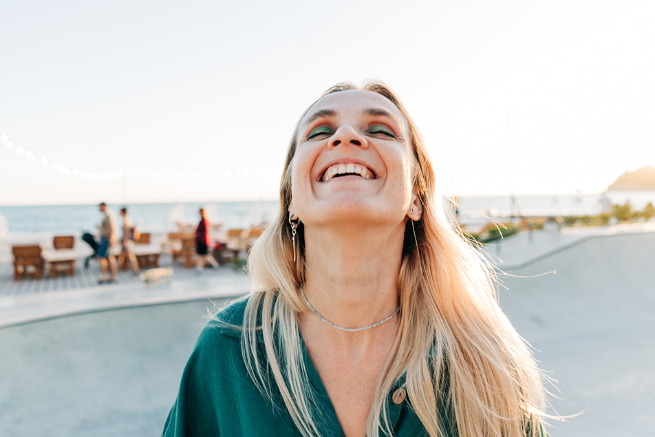 Happy woman laughing in the sunlight, representing confidence and emotional wellbeing after labiaplasty surgery
